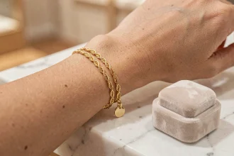 Bracelet femme en or fin avec chaîne torsadée et pendentif posé sur un écrin en velours et marbre blanc